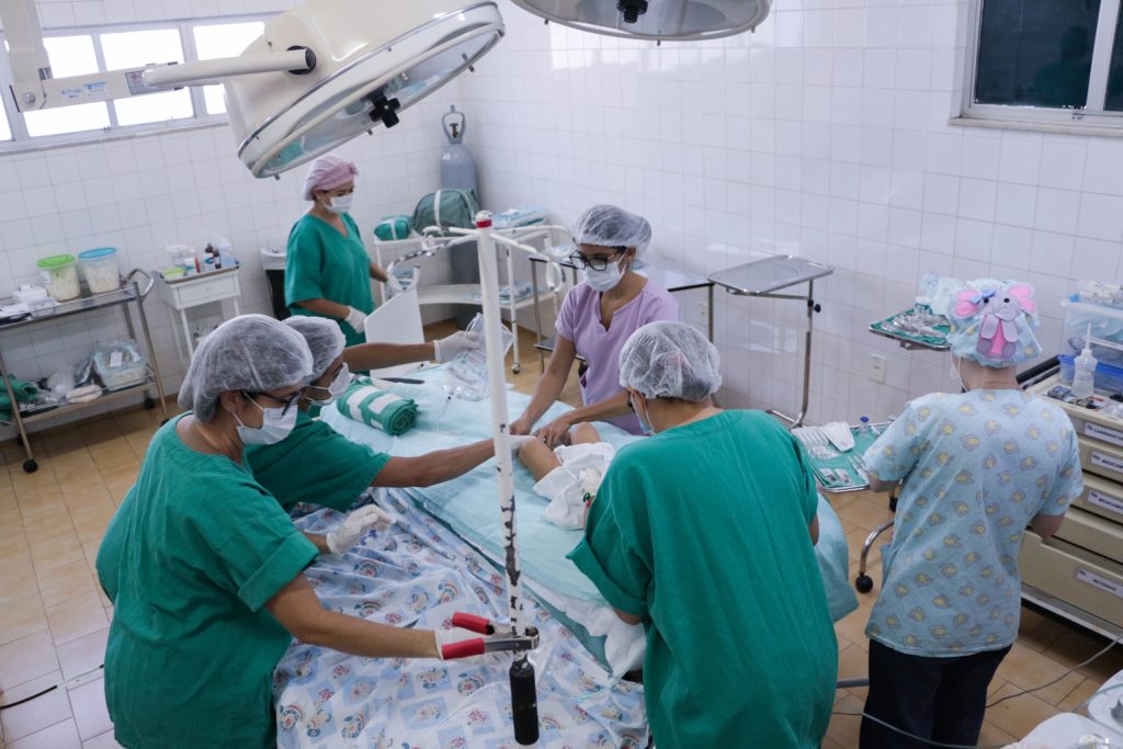 Sala de cirurgia com seis pessoas em volta preparando uma das crianças para a cirurgia