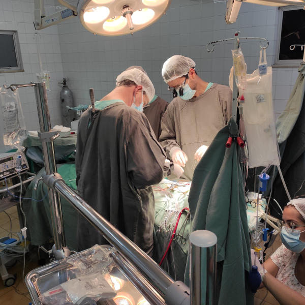 Imagem do centro cirúrgico e da equipe médica realizando procedimento na mesa de cirurgia.